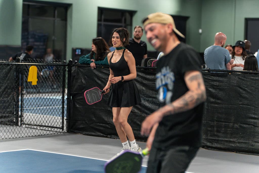Players on the indoor pickleball courts at At Fault Dallas with spectators watching from courtside